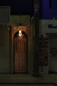 大阪・天満のBAR ALBAの入り口。温かみのあるランプが灯る隠れ家的なバーの扉 Entrance of BAR ALBA in Osaka Tenma, a hidden gem with a warm-lit wooden door.