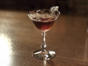 BAR ALBA（バー・アルバ）オリジナルカクテル『ダスク・アイランド』の写真。明るい木目のカウンターに映える赤いチェリーが、カカオリキュールの甘苦さを連想させる一杯。
