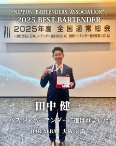 日本バーテンダー協会の顕彰式で「2025年度ベスト・バーテンダー」に選ばれた田中健一が、記念メダル手に笑顔で写っている。