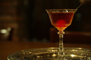 大阪・天満のBAR ALBAで味わう、赤褐色に輝くクラシックなマンハッタンカクテル。シンプルな背景が一杯の存在感を引き立てる。