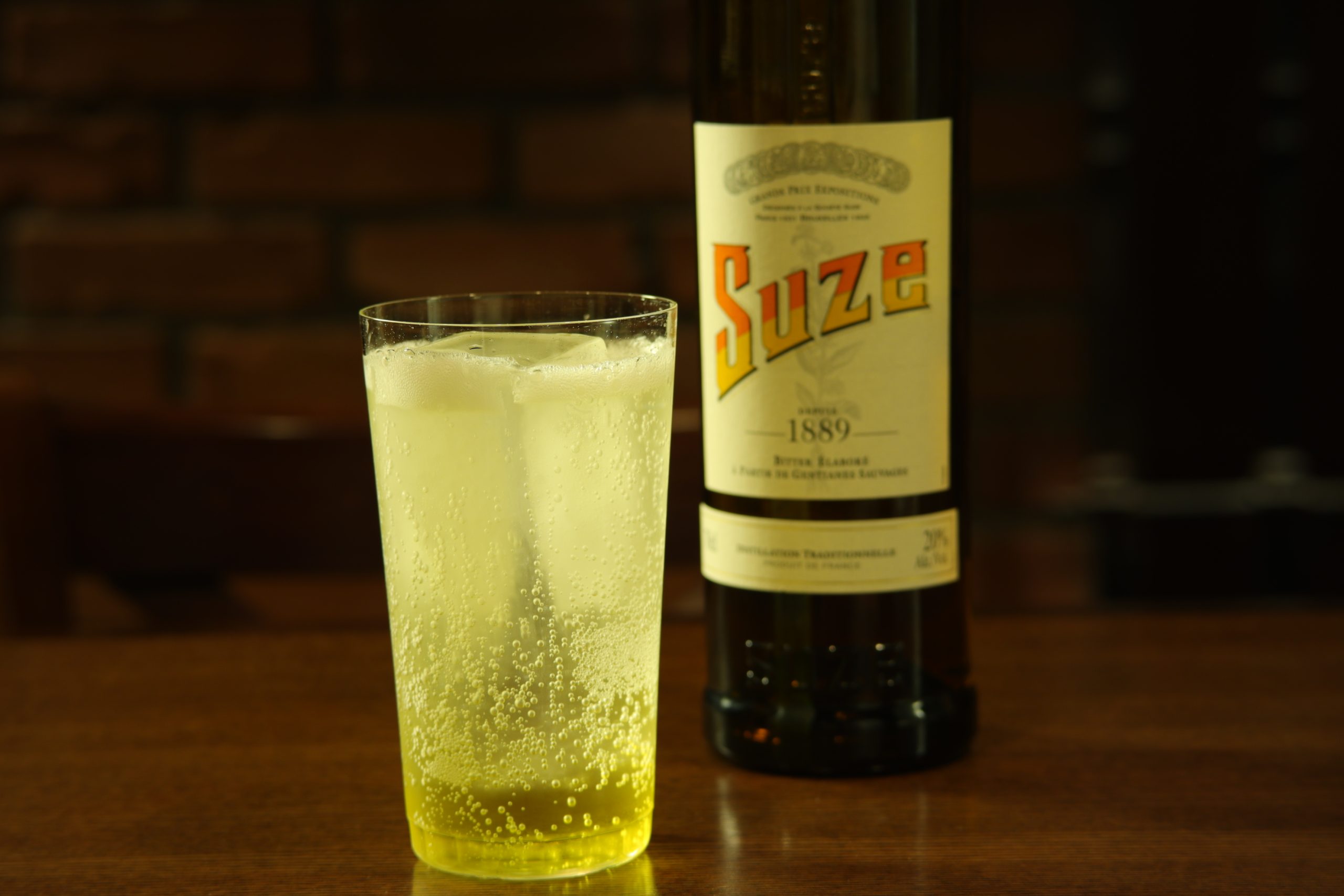 スーズのボトルとスーズ・トニックのグラス。明るい黄色のカクテルが夏らしい一杯。