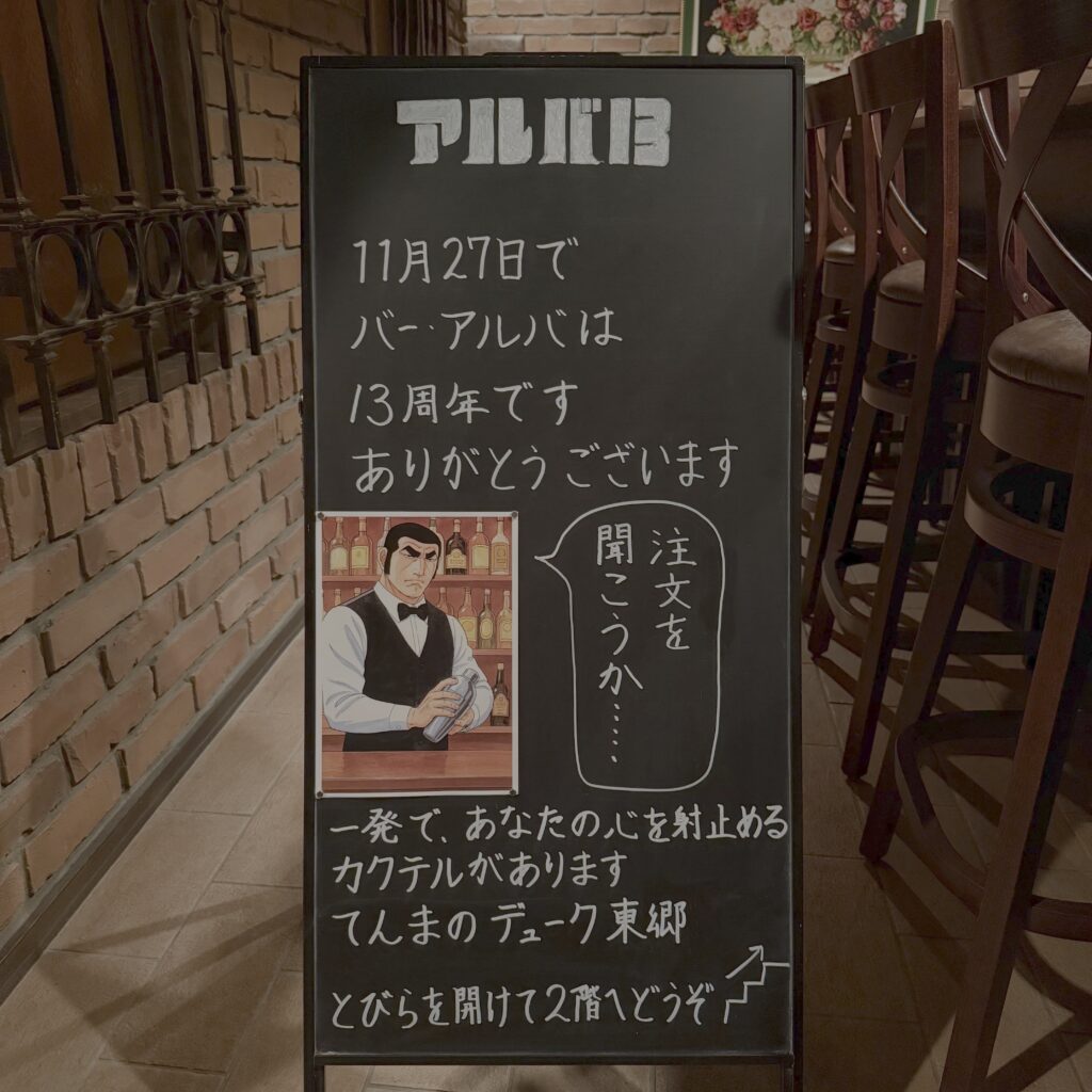 BAR ALBAの13周年を知らせる「アルバ13」黒板の写真。ゴルゴ13をオマージュしたイラストと、周年メッセージが描かれている。